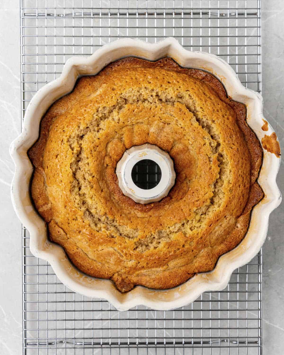 Baked walnut bundt cake in the white pan on a wire rack on a grey surface.