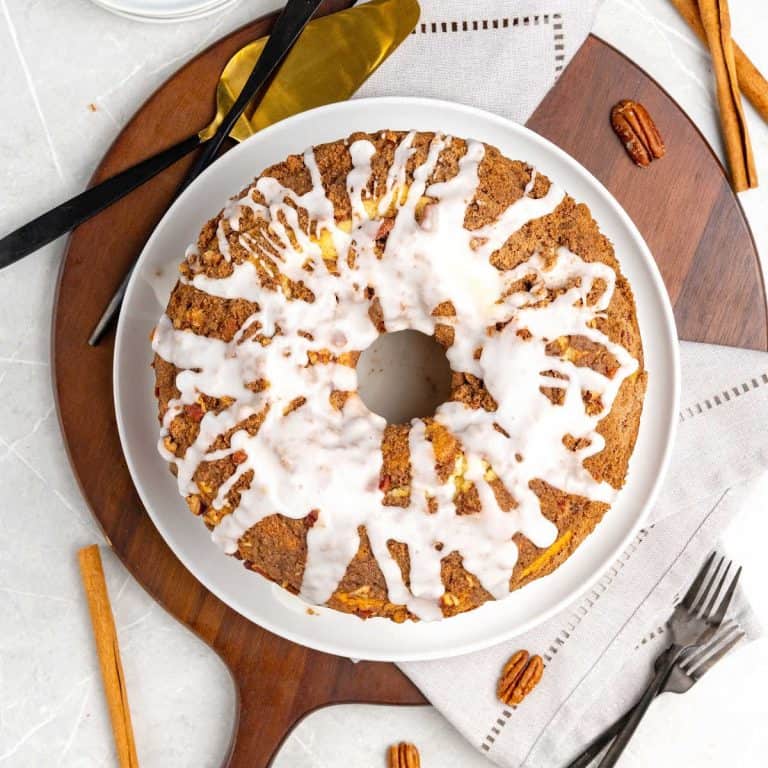 A glazed coffee cake on a white plate on a wooden board. White surface with forks and cinnamon sticks.