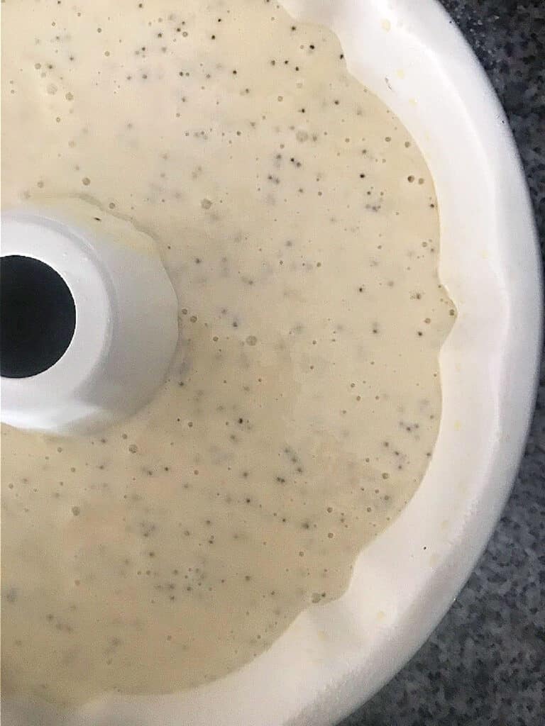 Partial view of white bundt cake pan with poppy seed batter.