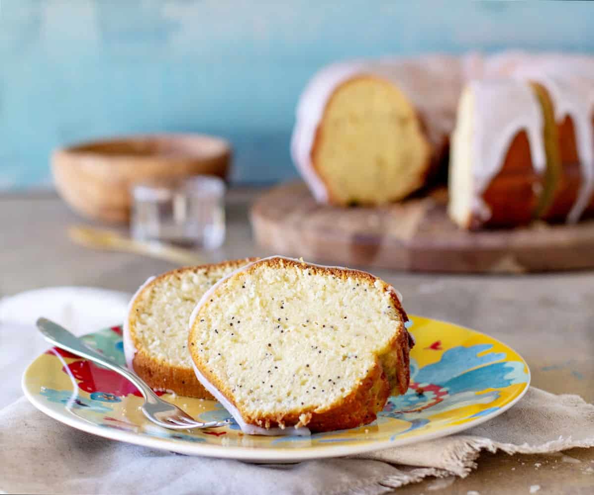 Slices of poppy seed bundt cake on a colorful plate. Blue background, glazed bundt cake. Gray surface. 