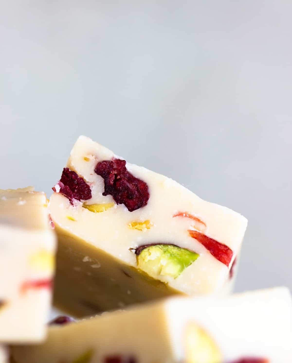 Close-up image of piece of white fudge with cranberries and pistachios, grey background