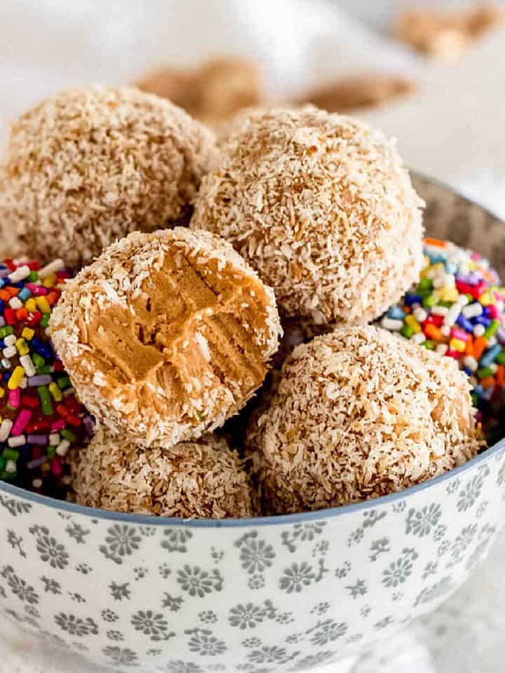 Dulce de leche truffles with coconut and sprinkles piled inside a grey bowl.