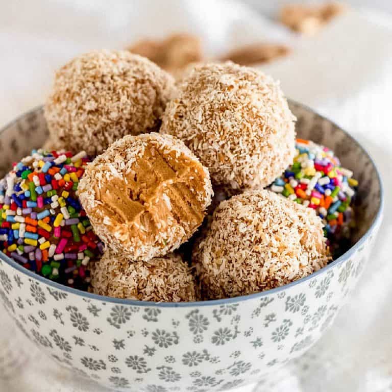 Dulce de leche truffles with coconut and sprinkles piled inside a grey bowl.