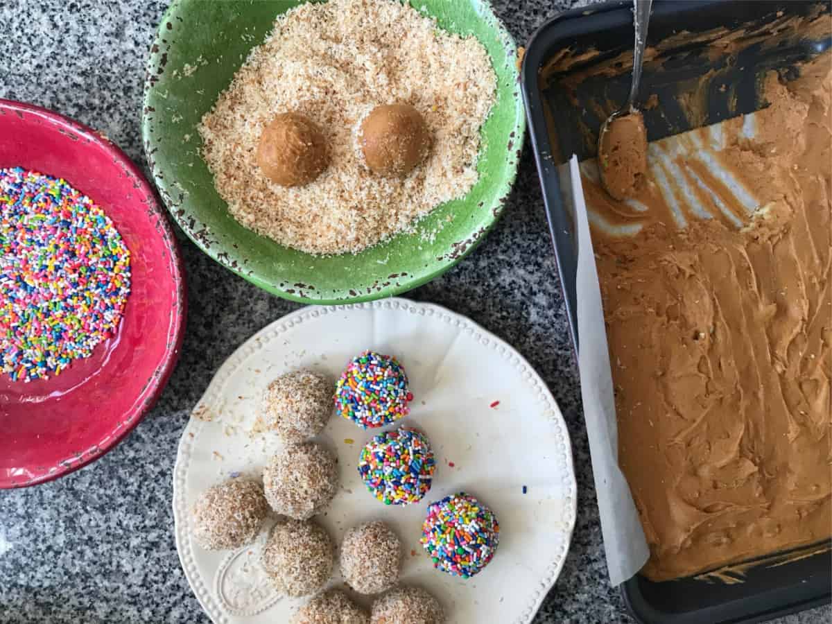 Grey marble with colorful bowls containing sprinkles and coconut, truffles and a pan with dulce de leche mixture. 