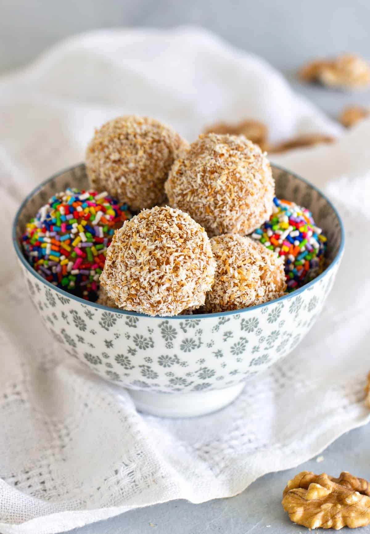 Dulce de leche fudge balls with coconut and sprinkles in a grey bowl. White grey background. 
