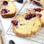 Close up of blackberry muffin loaf slice on a wire rack. White surface.