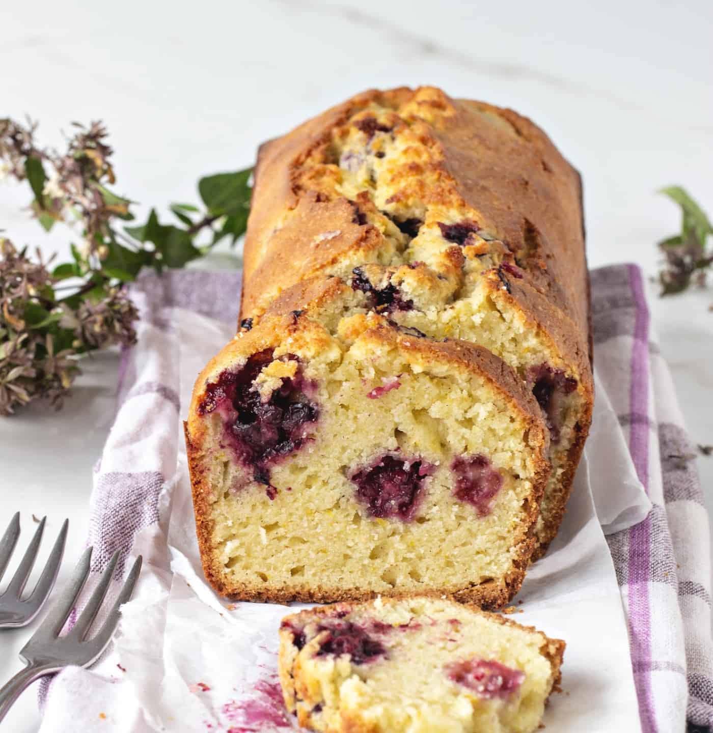 Loaf of sliced Orange blackberry cake, checkered kitchen towel, flowers