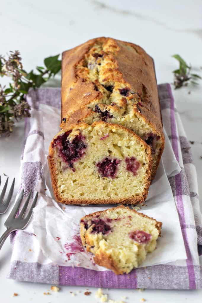 Slices and whole Orange blackberry muffin loaf, kitchen towel, forks, small flowers