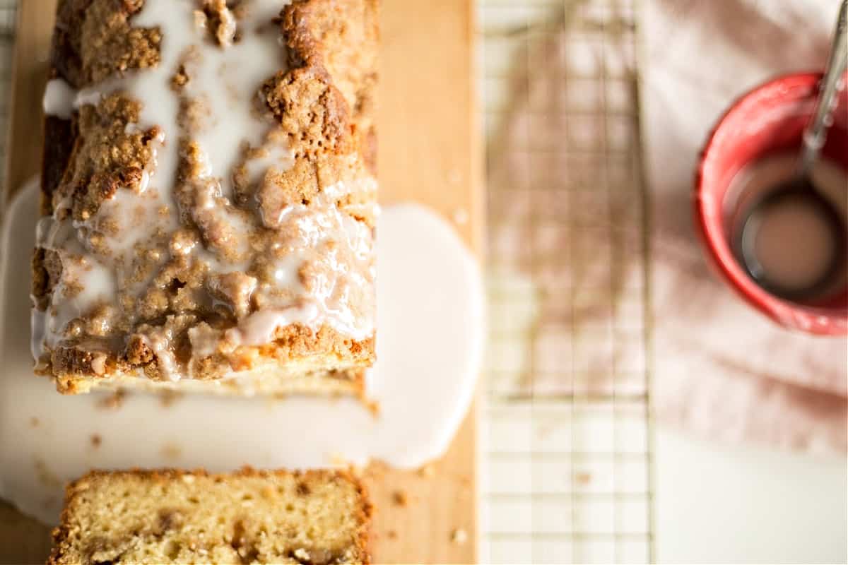 Top view of loaf cake drenched in sugar glaze, metal rack on white surface, red bowl