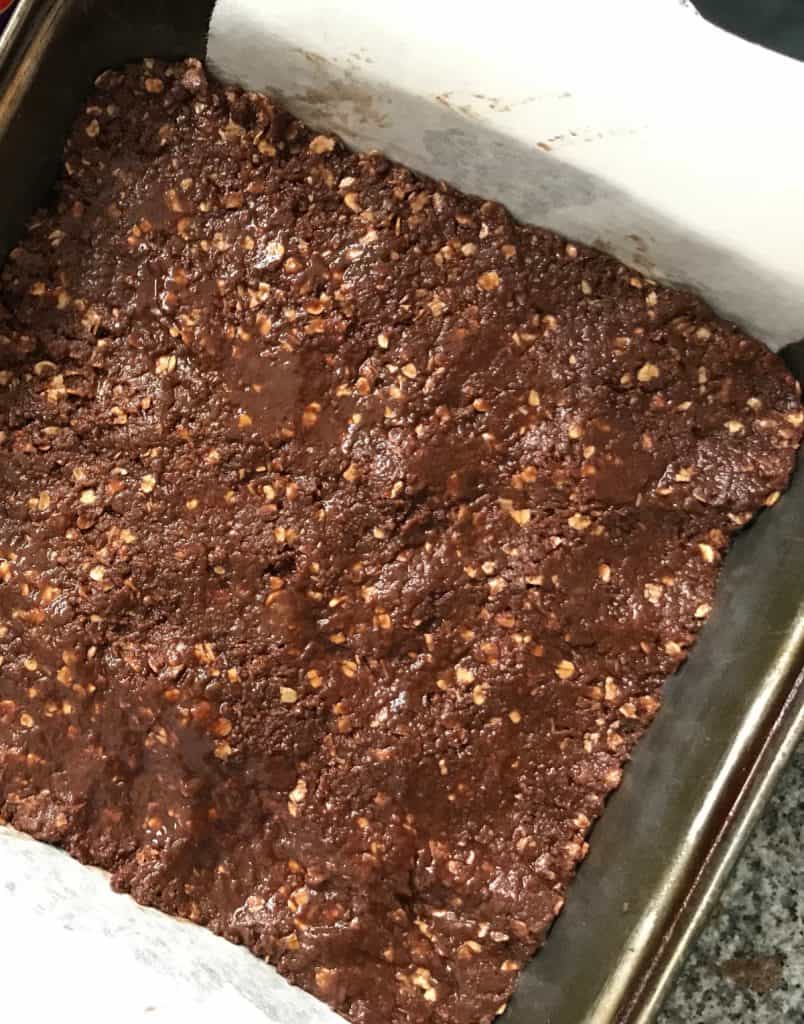 Raw mixture of chocolate and oat pressed onto metal pan with parchment paper