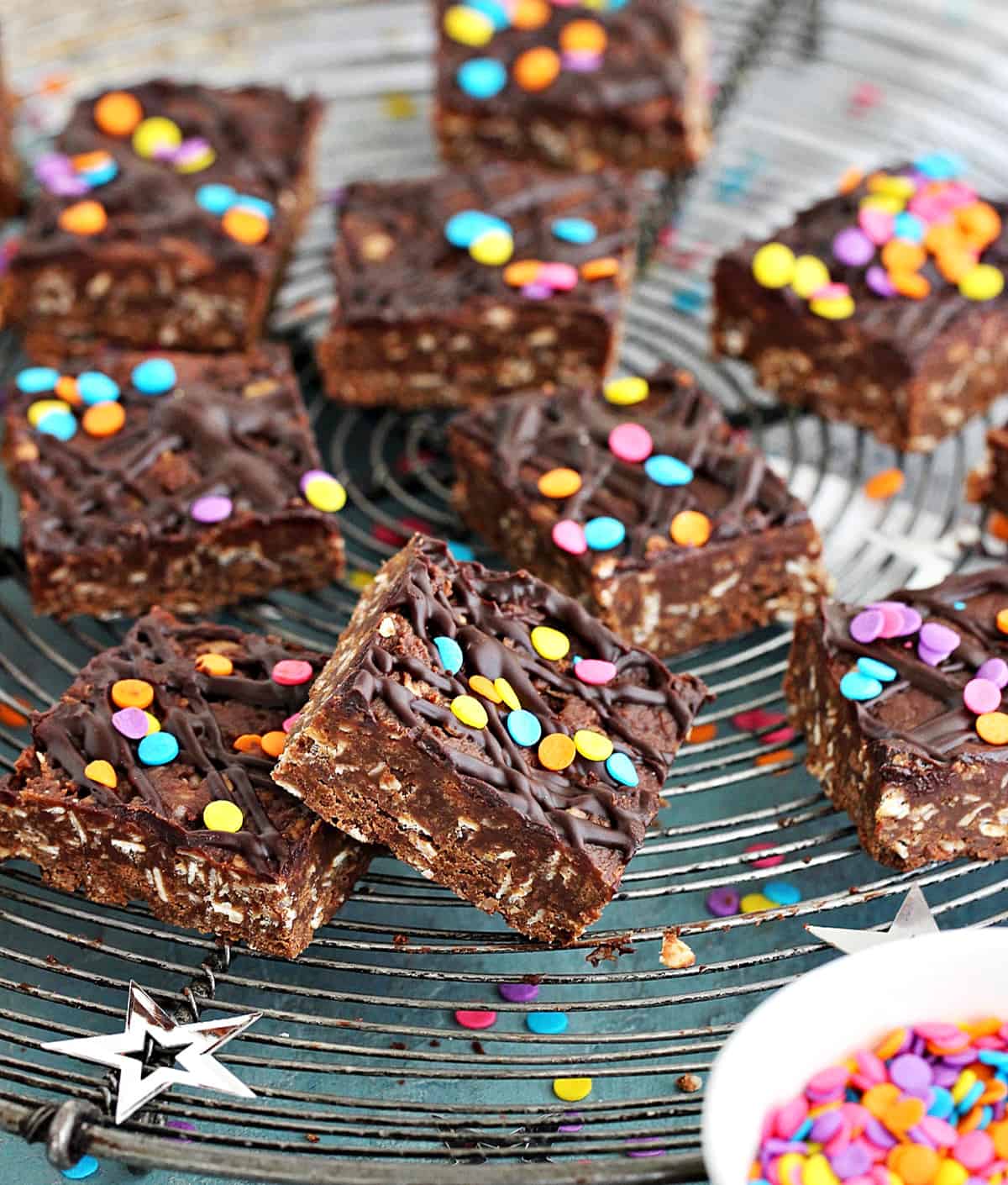 Chocolate oat squares on a wire rack with confetti, bluish background.