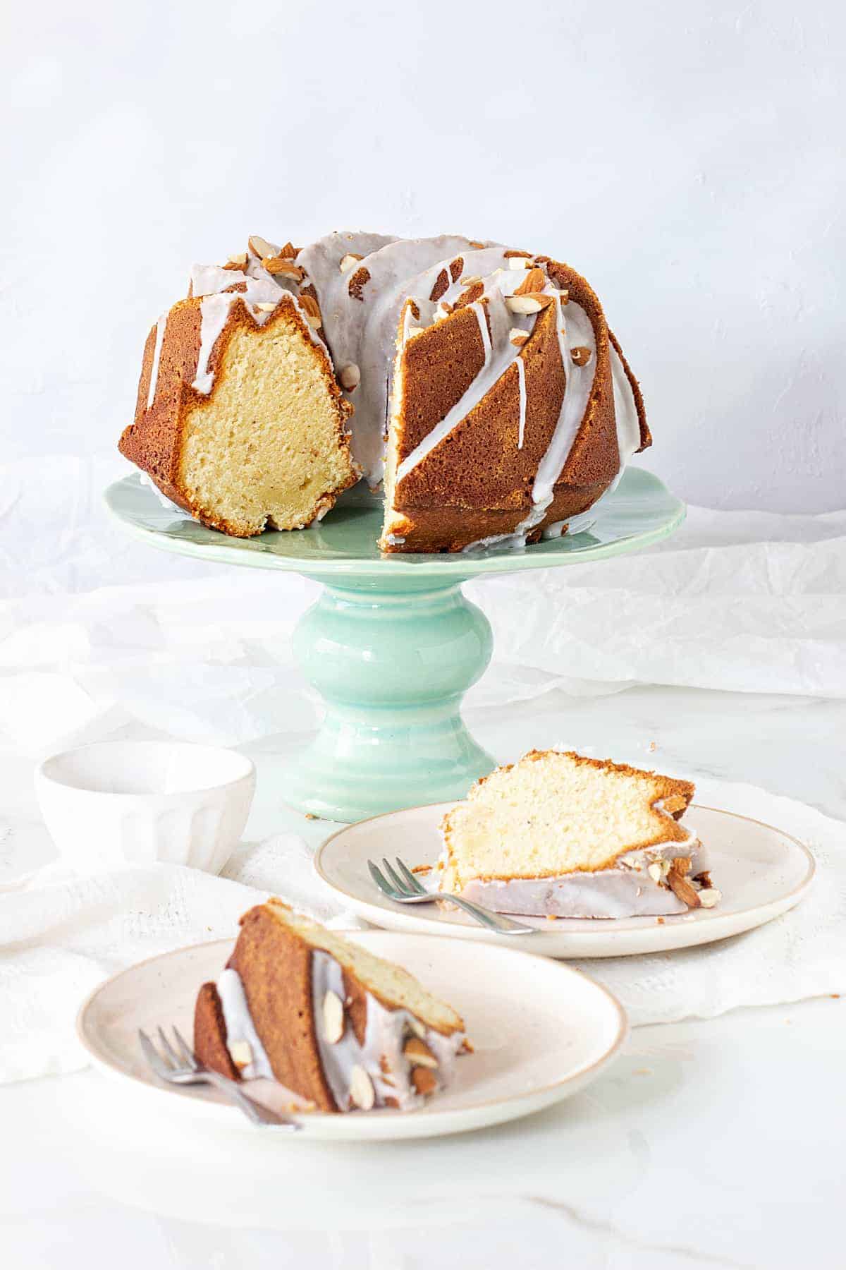 Bundt cake on a green cake stand, two slices on plates, forks, white surface