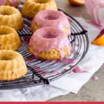 Blood orange cakes on wire rack, pink glaze dripping, white bowl, orange wedge