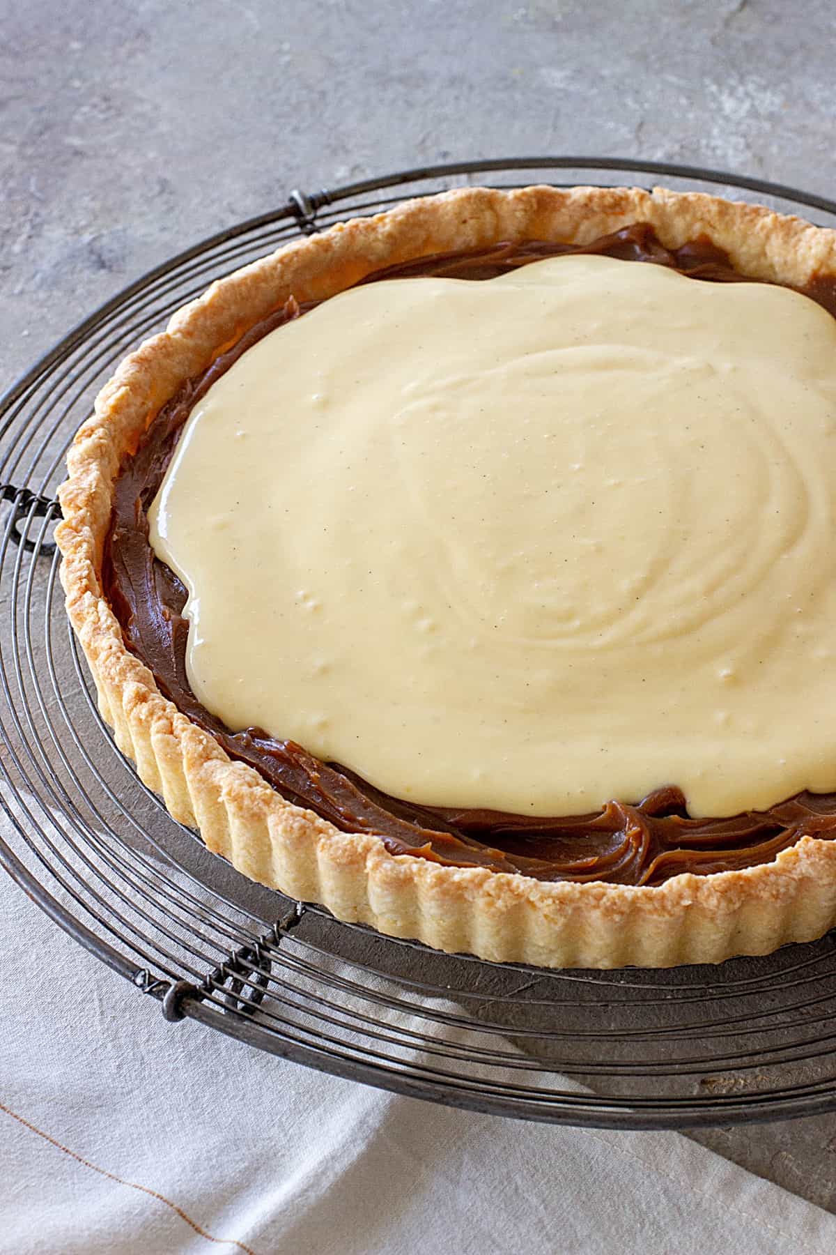 Coconut lemon tart with dulce de leche on a wire rack on a grey surface.