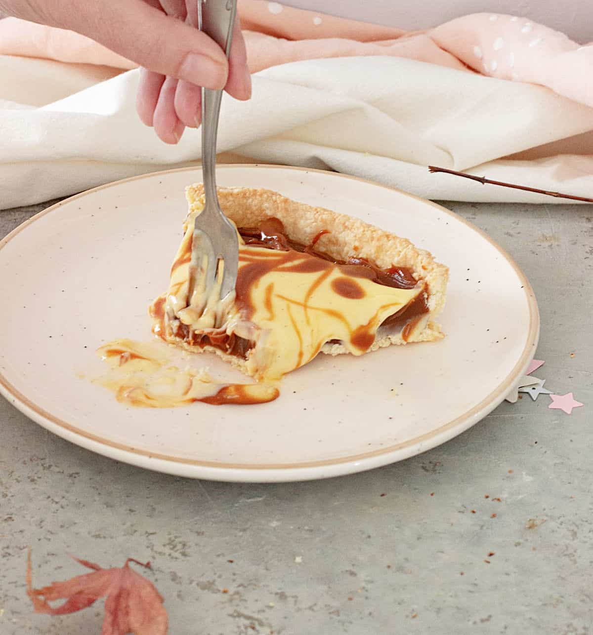 A forked slice of lemon dulce de leche tart on a pink plate on a grey surface.