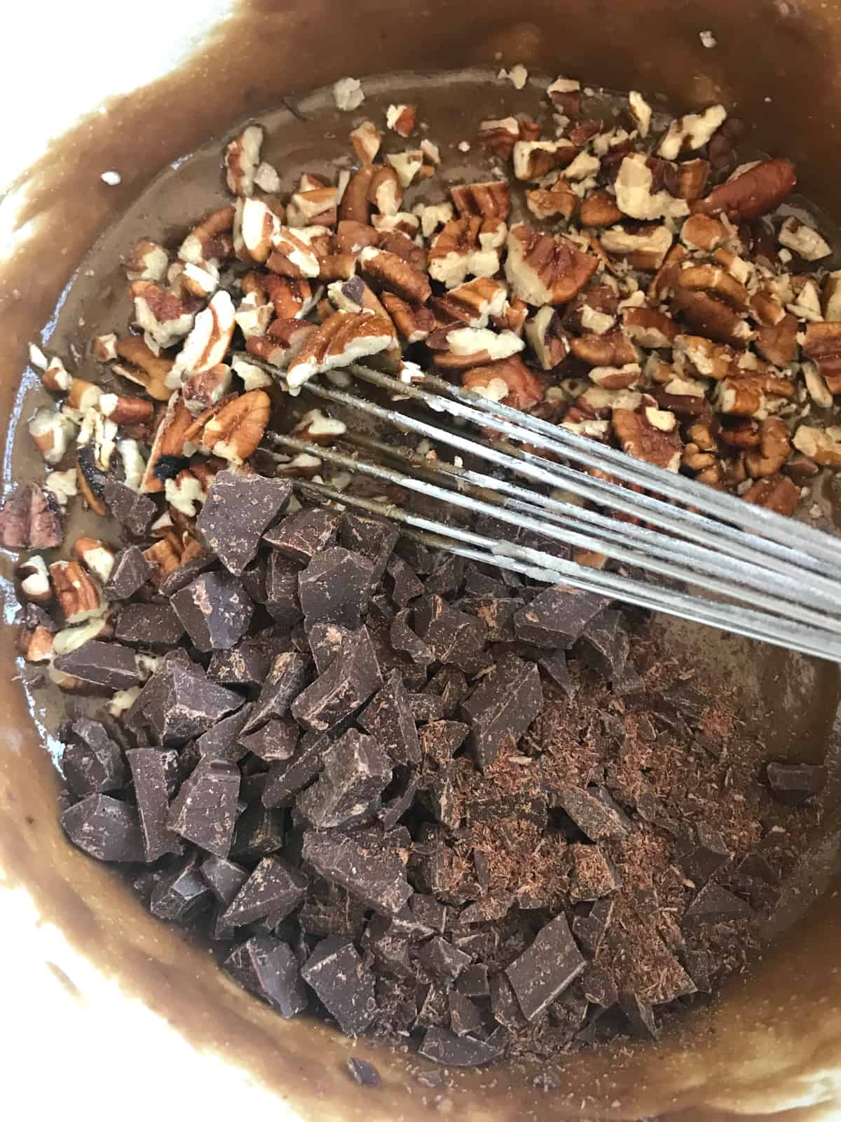 Chocolate chunks and chopped pecans in bowl with blondie batter and whisk. 