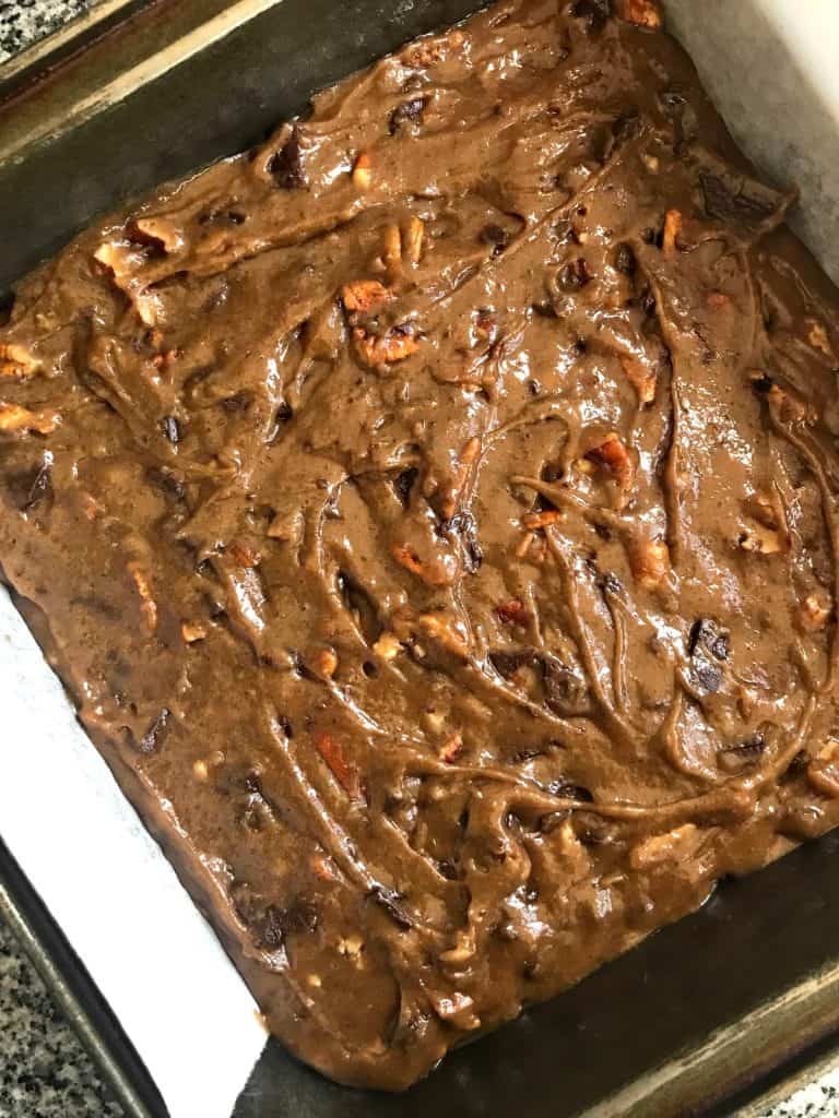 Ground cookie blondies with chips and nuts in a square metal pan before baking. 