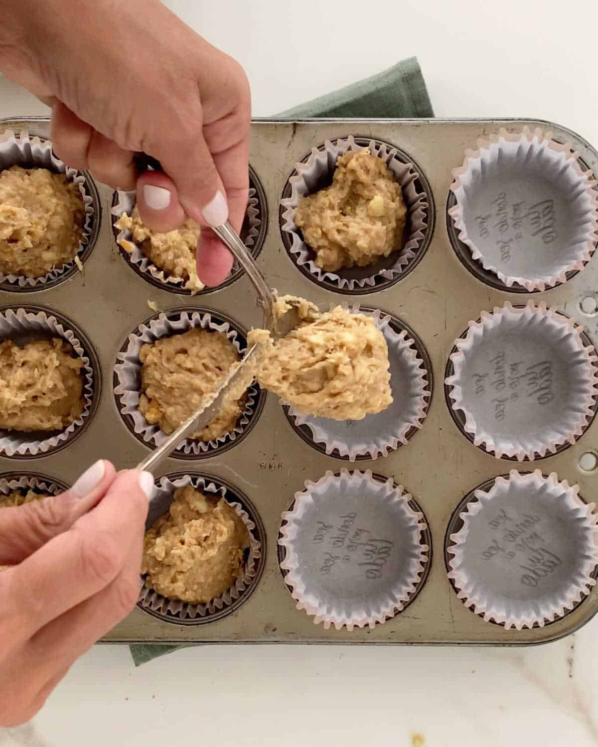 Filling paper liners with banana muffin batter. Metal pan on white marble surface. 