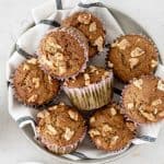 Close up of piled banana nut muffins on a striped cloth with a light grey background.