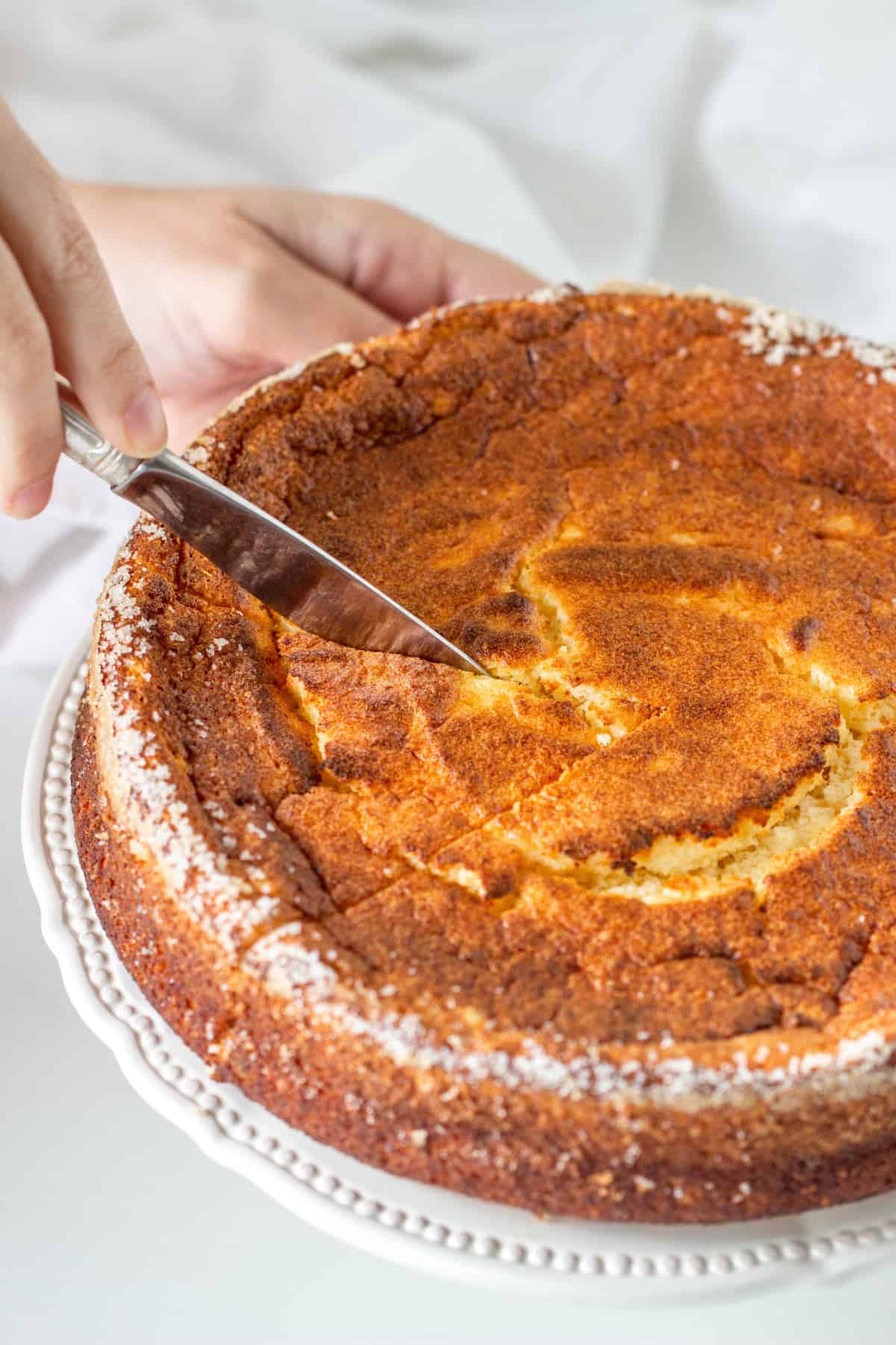 Cutting a slice of orange ricotta cheesecake on a white plate with a silver knife. 