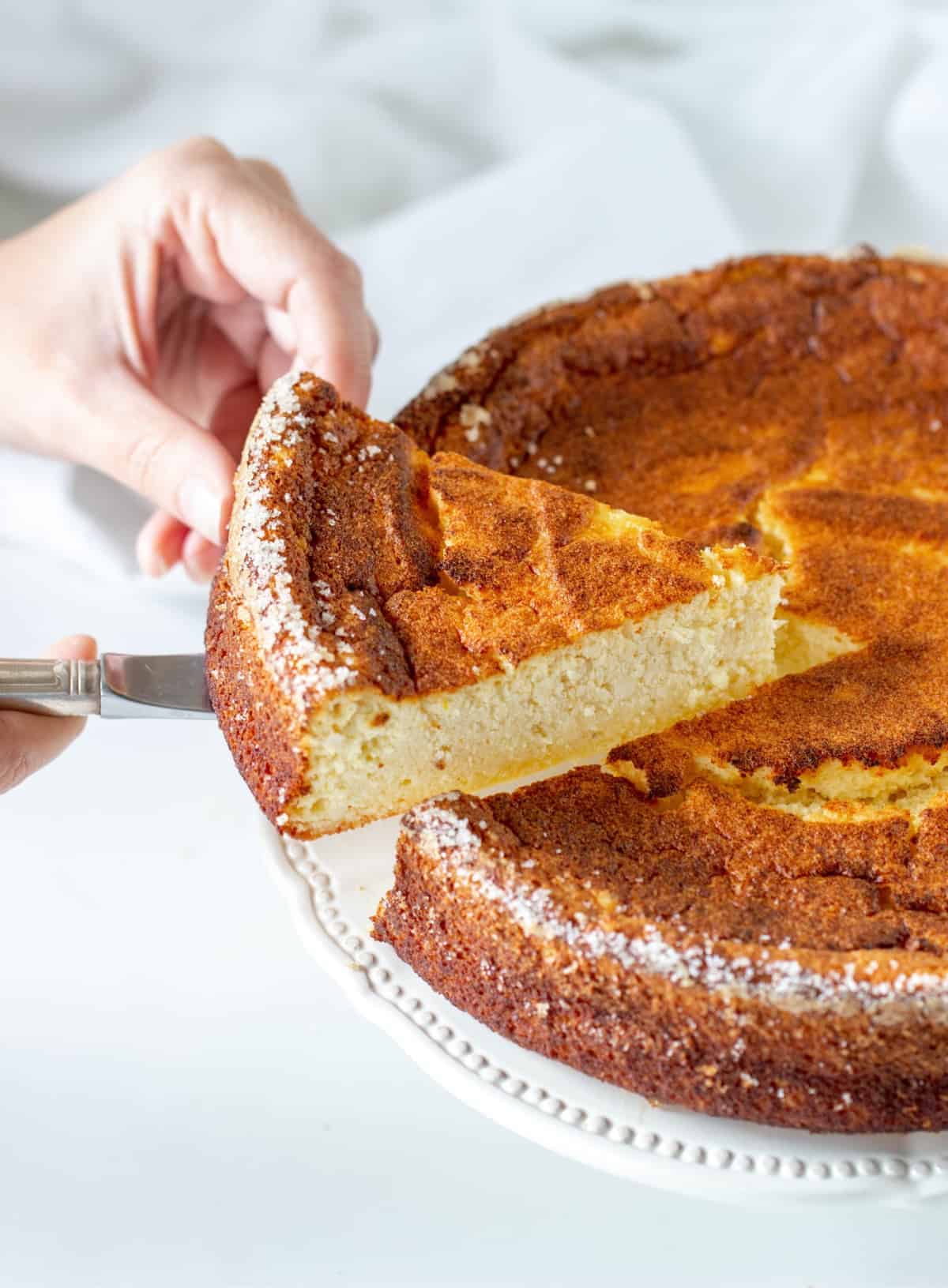 Whole Orange ricotta cheesecake and slice being cut, white background.