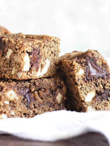 Squares of cookie blondies with chocolate chunks on a white cloth and white background.