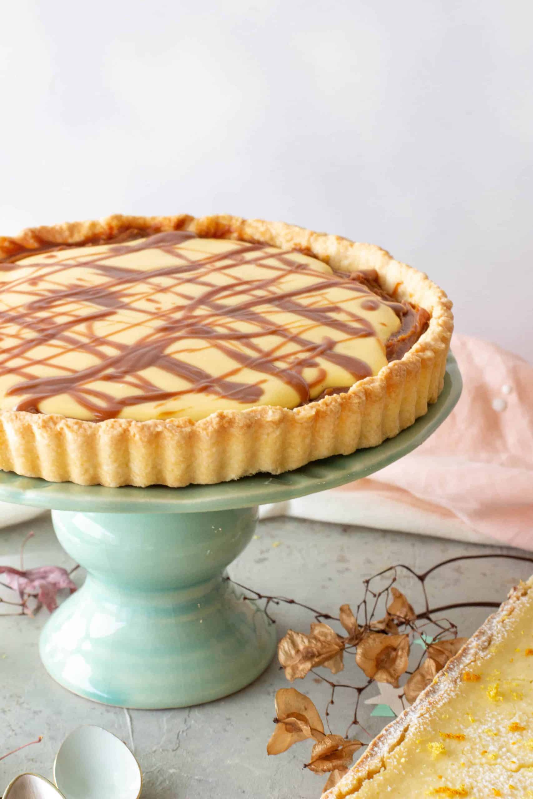 Lemon tart with dulce de leche on a green cake stand, grey surface, dried leaves around. 