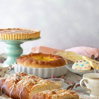An Easter brunch table with a pie on a stand, cookies, braided breads, a lemon ricotta pie.