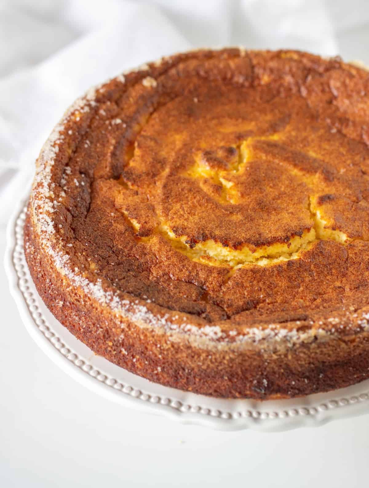 Whole ricotta cheesecake on a white plate on a white table.