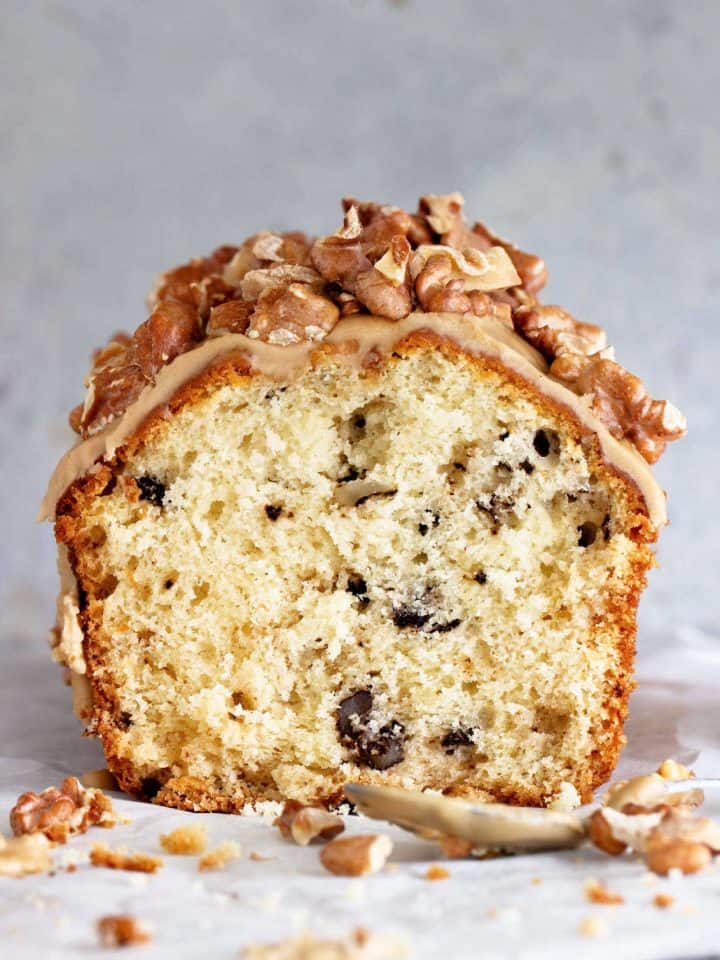Front view of half walnut loaf with glaze and nuts on top. Grey surface and background.