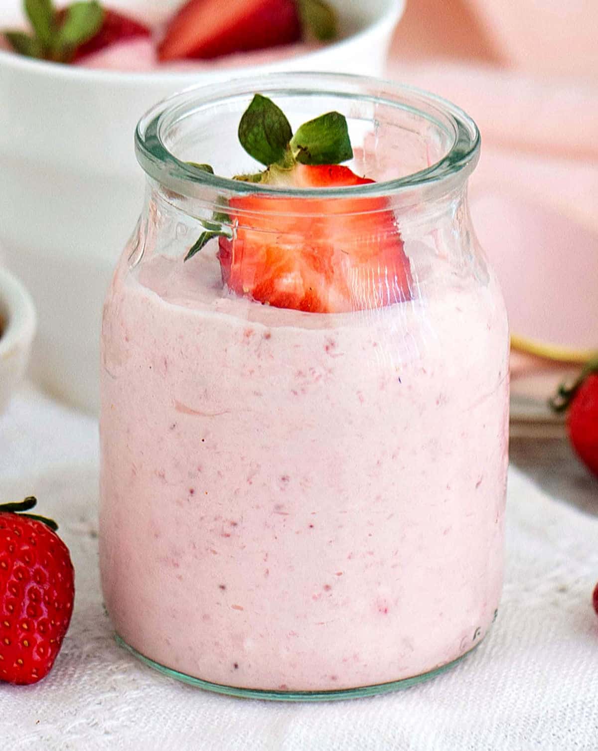 Close up of glass jar with strawberry cream dessert and half berry on top