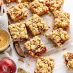 Several plum crumb bars on parchment paper. White surface, coffee cup. Top view.