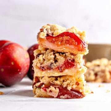 Stack of plum crumble bars. Whitish surface and background. Whole plums.