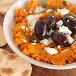 Bowl of carrot dip, black olives, goat cheese and crackers