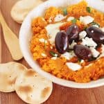 Bowl of carrot dip, black olives, goat cheese and crackers.