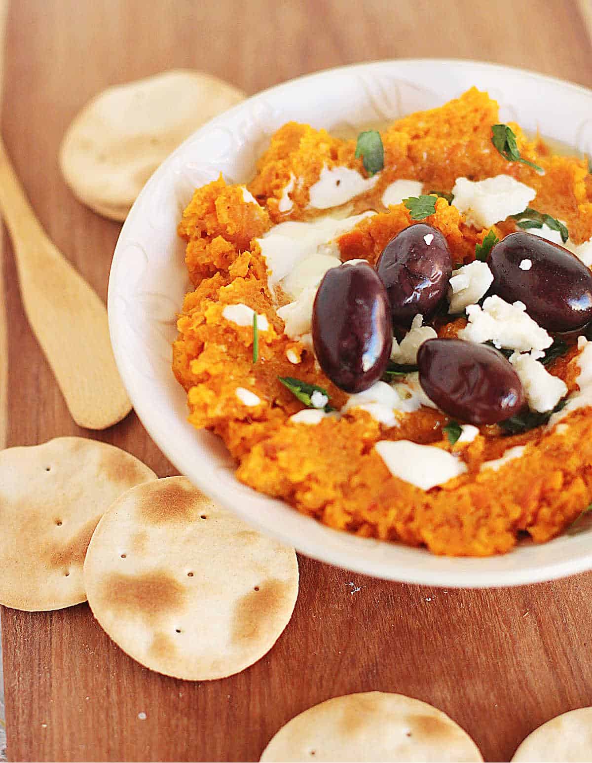 Bowl of carrot dip, black olives, goat cheese and crackers.