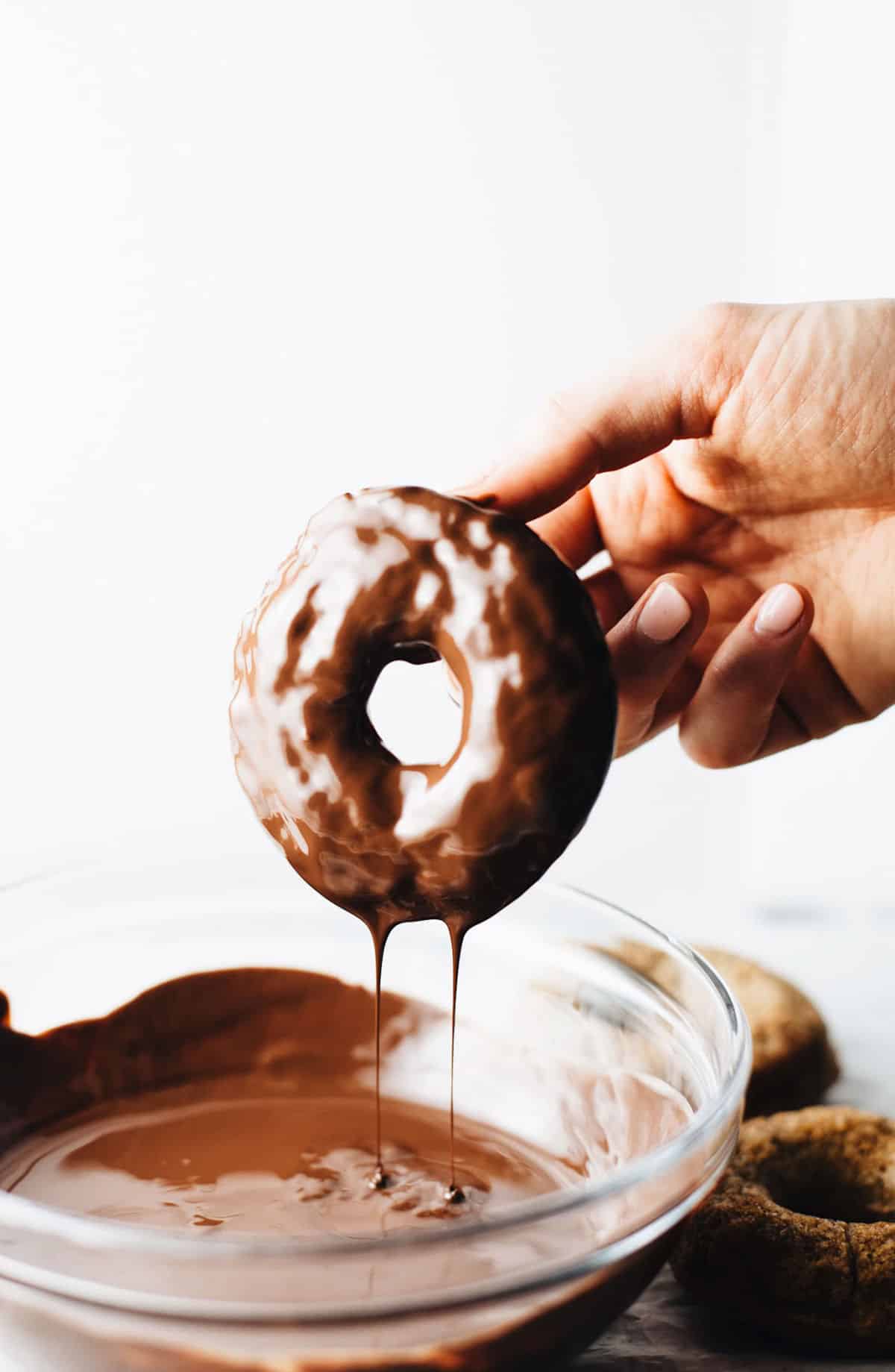 Hand with banana doughnut being dipped in chocolate glaze