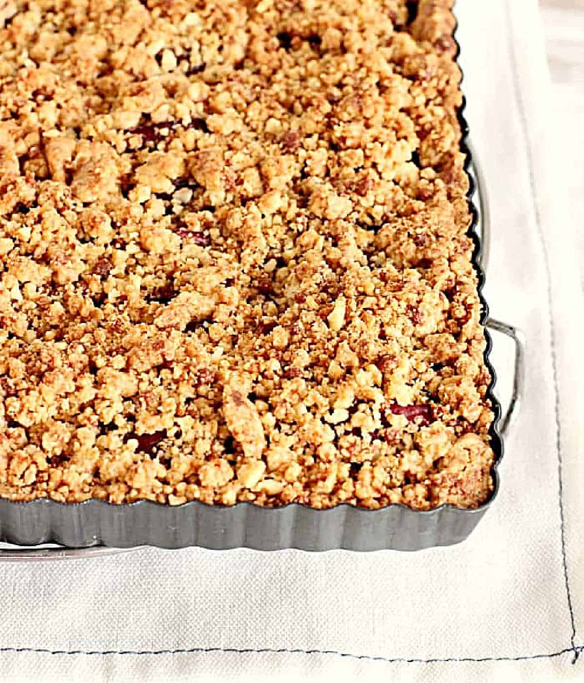 Top view of crumble topped square tart pan on a white cloth.