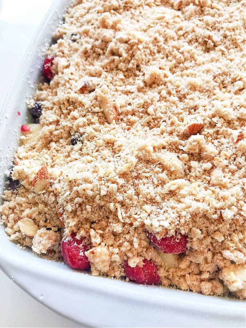 Unbaked fruit crumble in a white ceramic dish. Close up image.