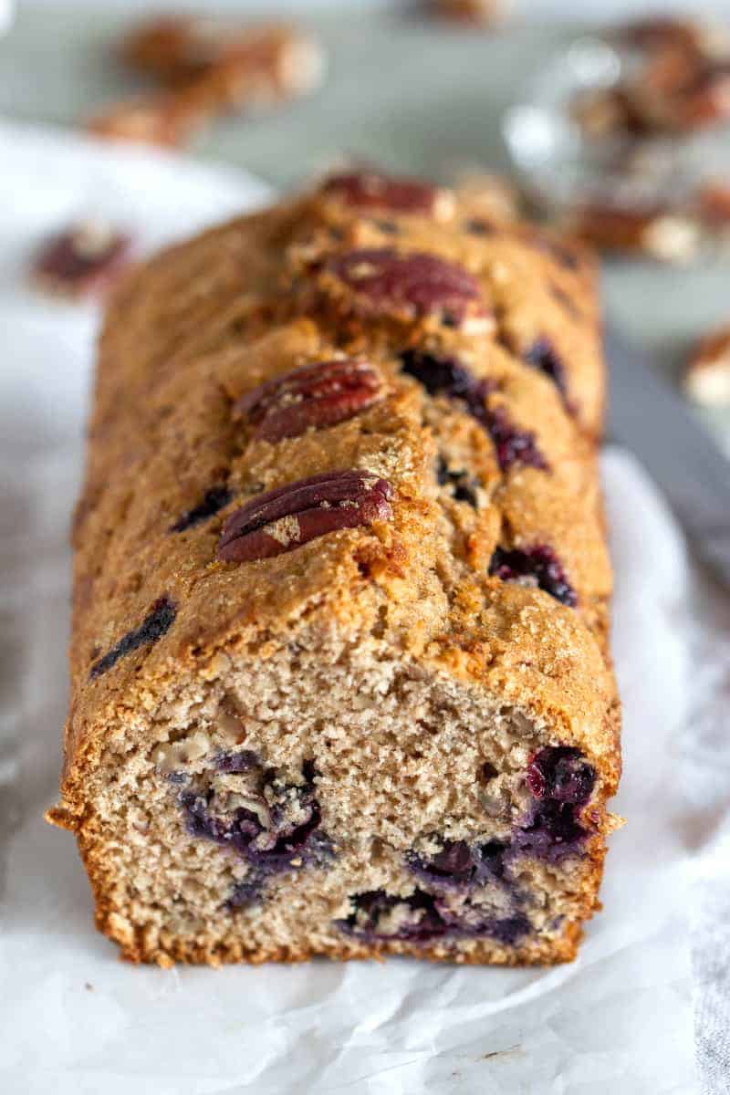 Pecan studded blueberry loaf cake, white surface, scattered pecans