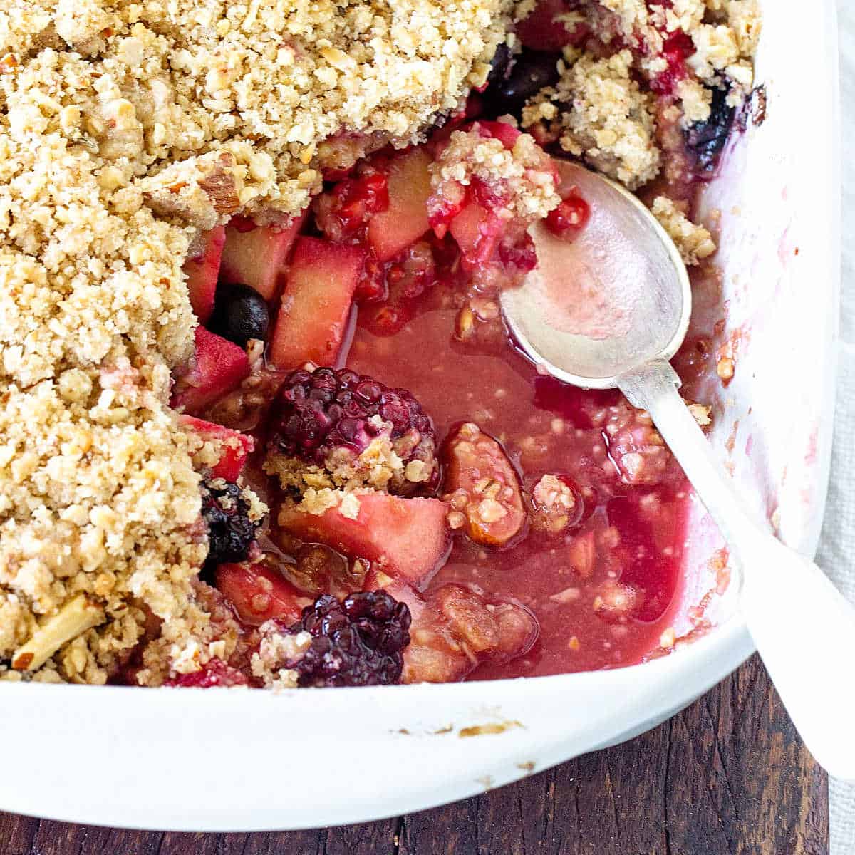 Partial view of eaten fruit crumble on a rectangular white dish with a silver spoon inside.