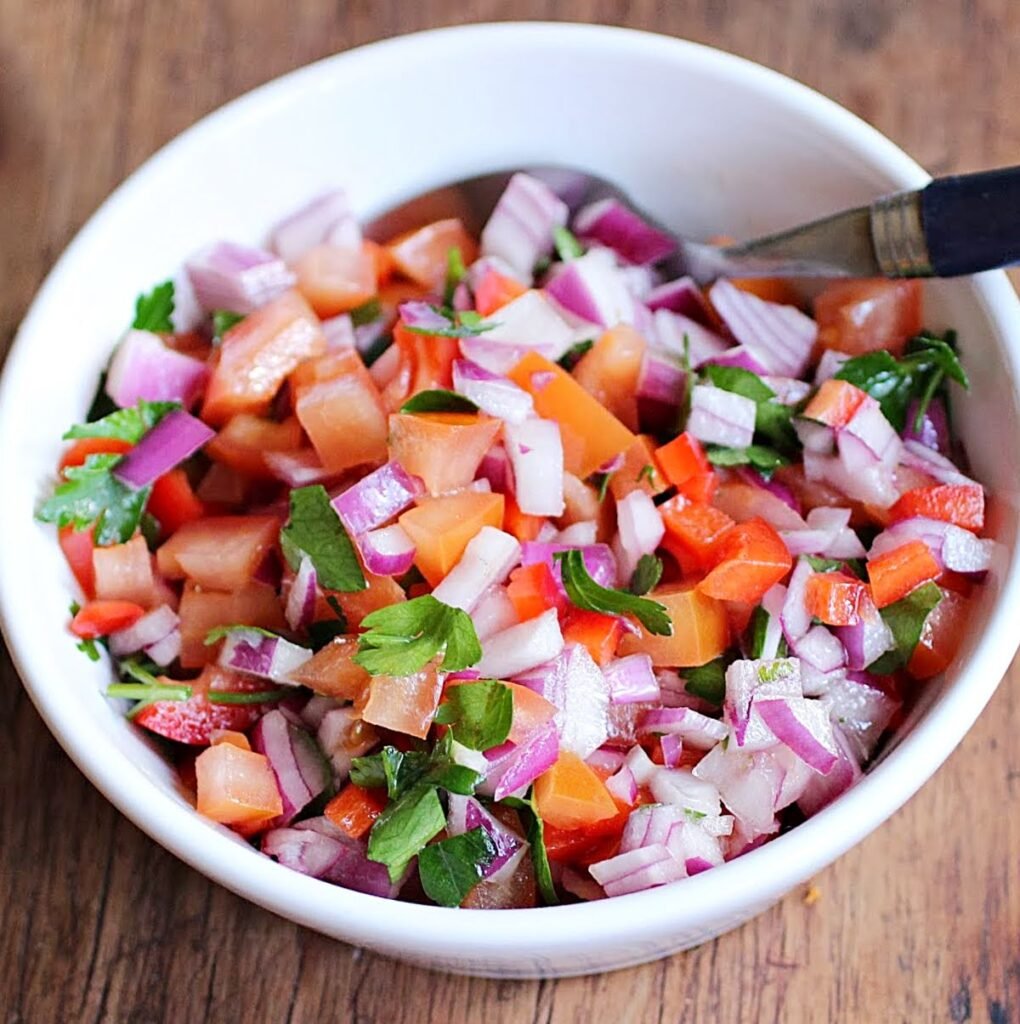 White bowl with tomato, red onion and parsley salsa. Wooden surface. A spoon.