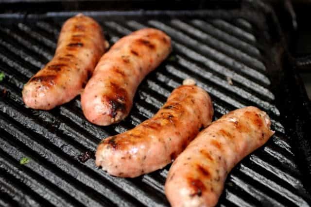 Butterflied chorizos being grilled in a cast iron ridged skillet.
