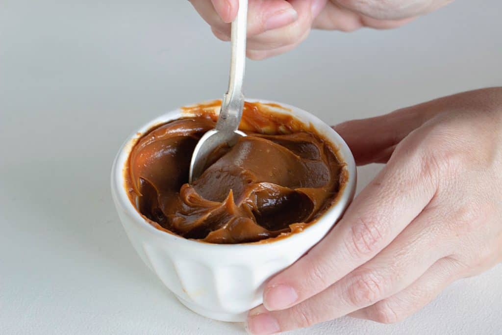 White bowl of Dulce de leche, hands and spoon