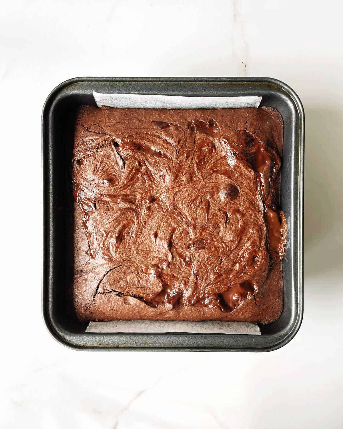 Top view of square pan with baked brownies with dulce de leche. White marble surface. 