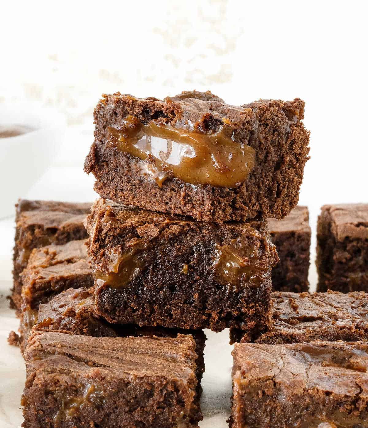 Stack of dulce de leche brownies with rows of more brownies. White background. 