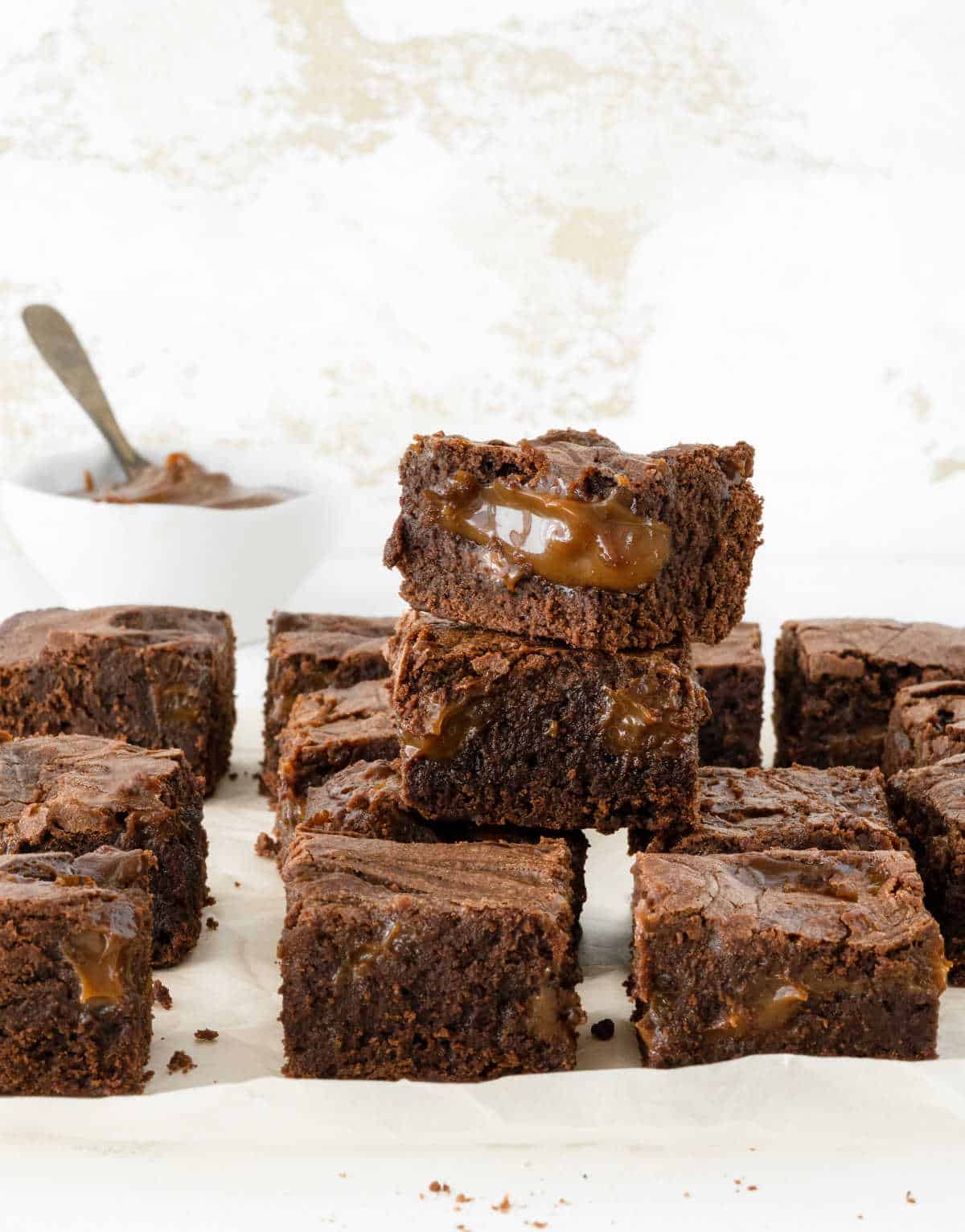 Rows and stack of brownies with dulce de leche on beige parchment paper and white background. 