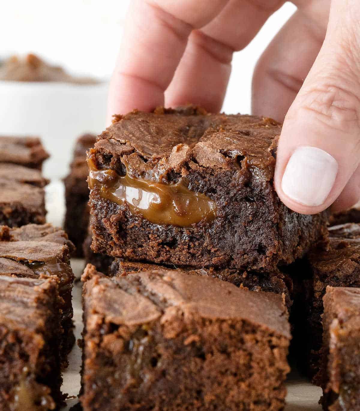Hand grabbing a dulce de leche brownie from a stack.