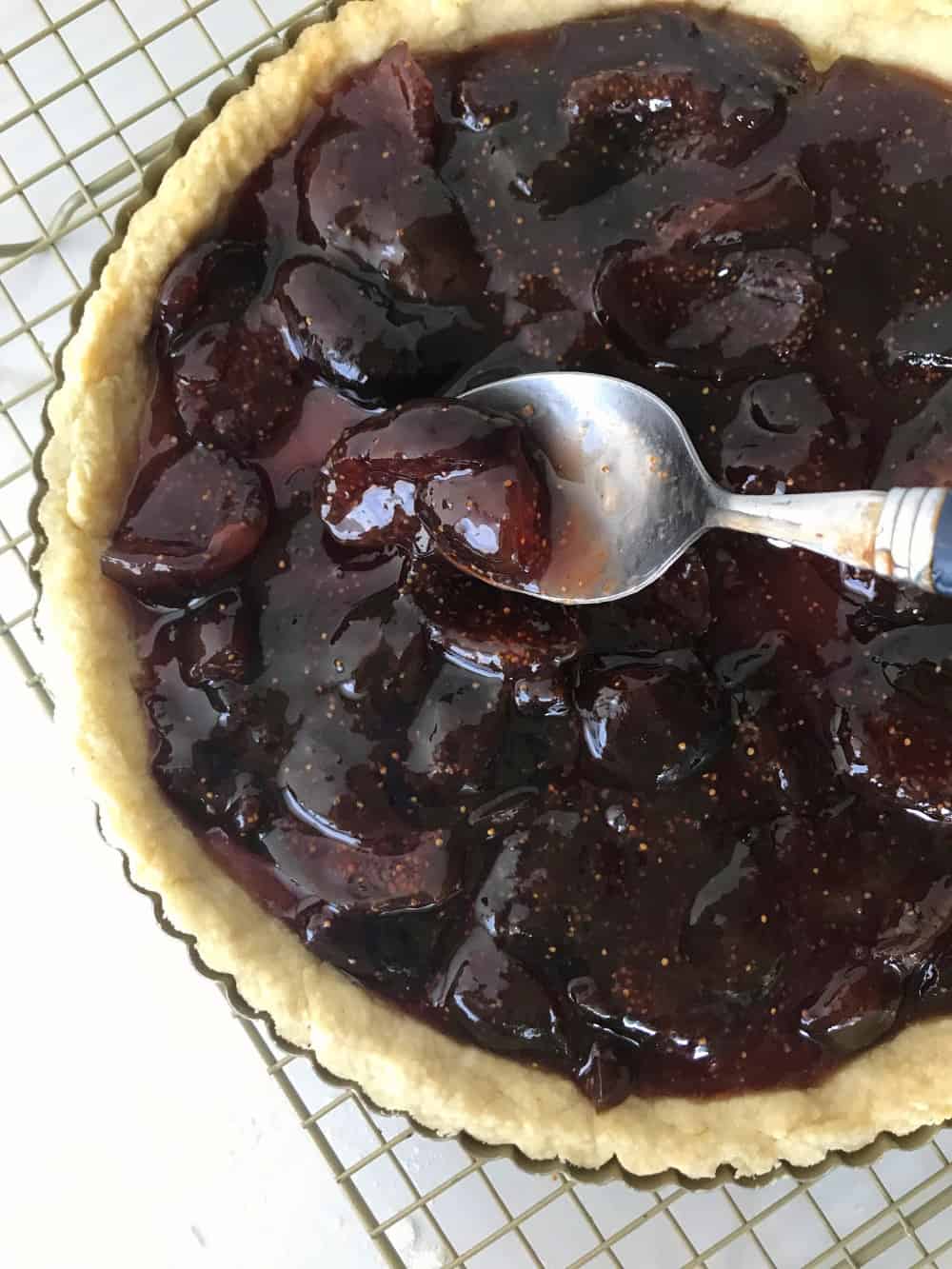 Pie with homemade fig jam on wire rack, spoon