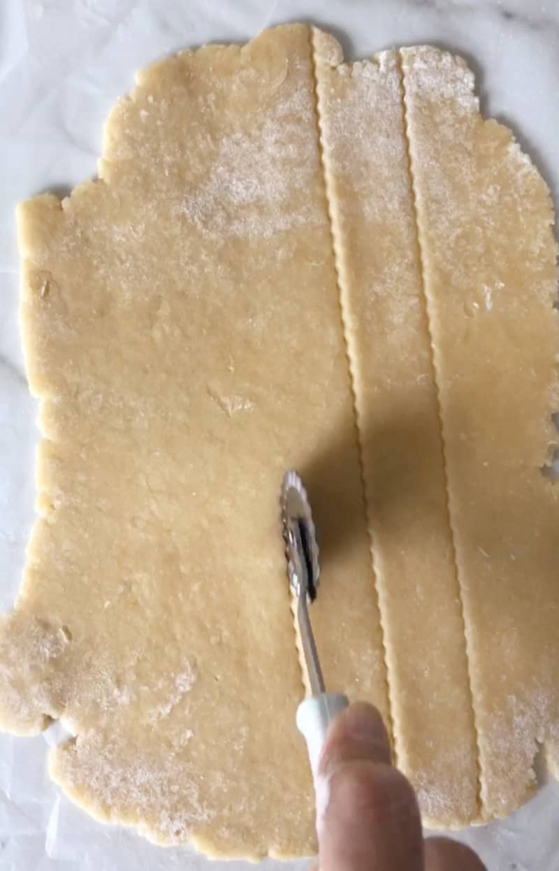 Cutting strips of sweet dough rolled on white surface.